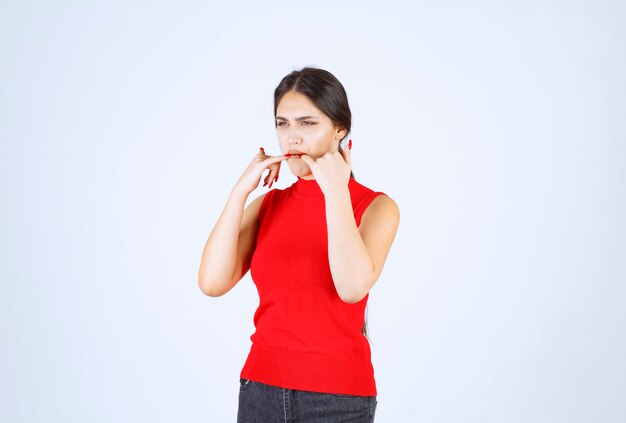 Girl in red shirt putting hands into her mouth and whistling.