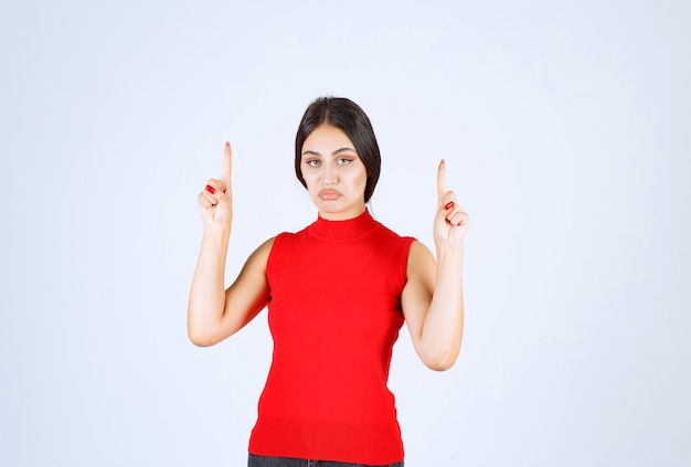 Girl in red shirt raising hand and pointing above.