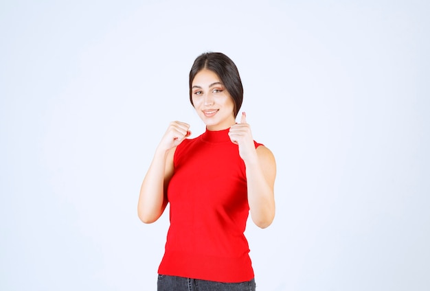 Girl in red shirt showing enjoyment hand sign.