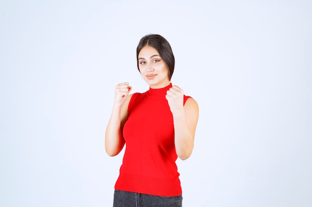 Ragazza in camicia rossa che mostra i suoi muscoli e pugni del braccio.