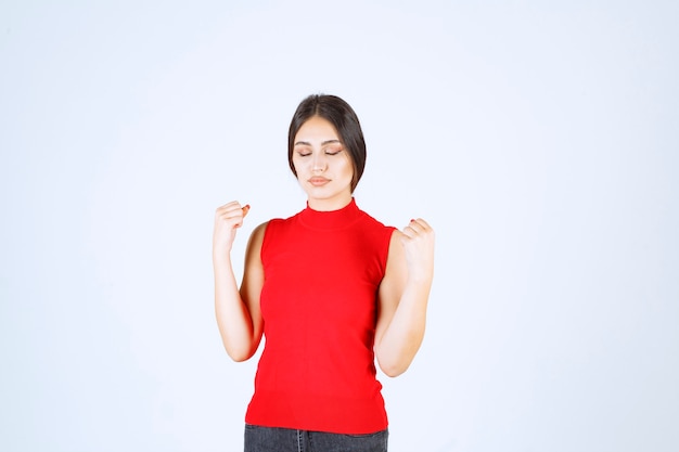 Ragazza in camicia rossa che mostra i suoi muscoli e pugni del braccio.