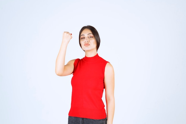 Girl in red shirt showing her arm muscles and fists.