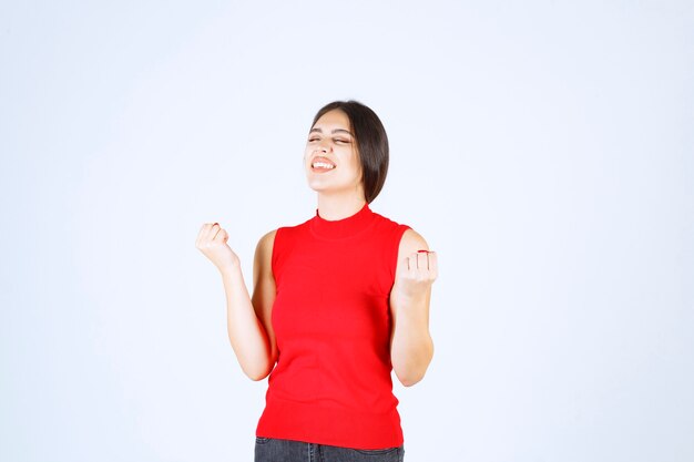 Girl in red shirt showing her arm muscles and fists.