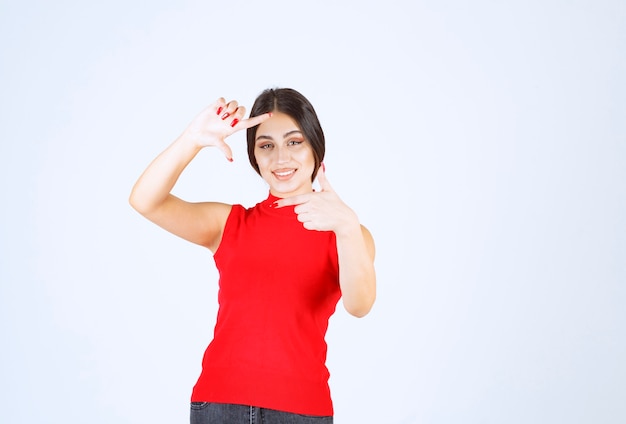 Girl in red shirt showing photo capturing hand sign.