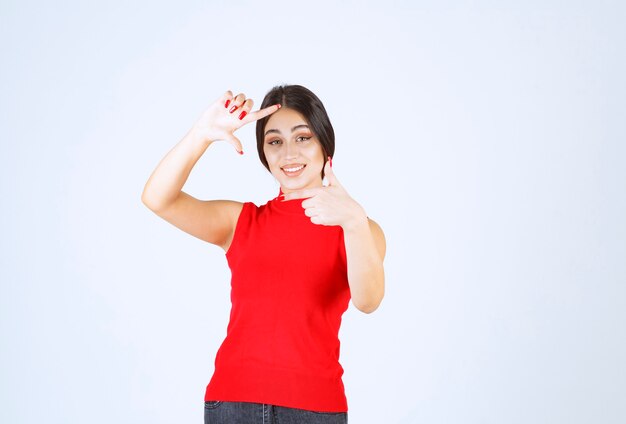 Girl in red shirt showing photo capturing hand sign.