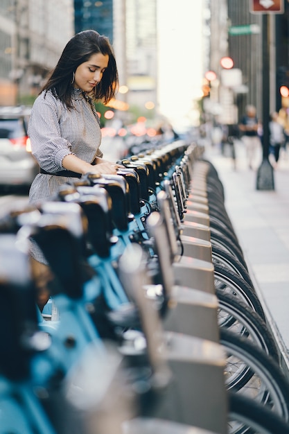 Free photo girl renting a city bike from a bike stand