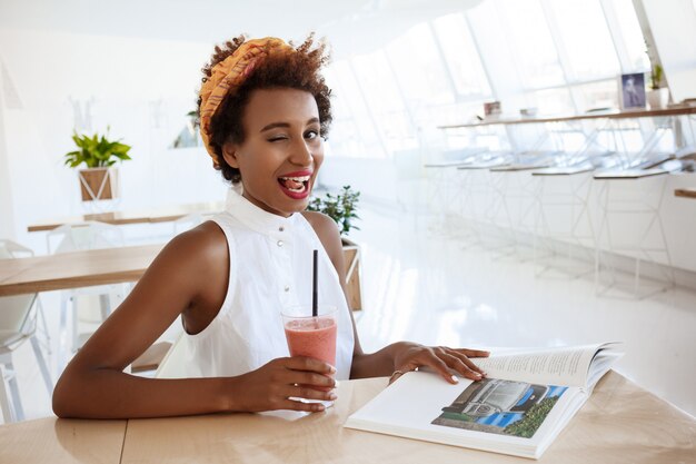 Girl resting in cafe drinking smoothie smiling winking showing tongue