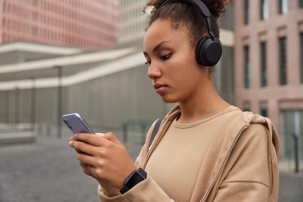 girl rests after training uses phone for chatting online downloads songs to playlist listens audio from cell player connected to cellular application poses in city