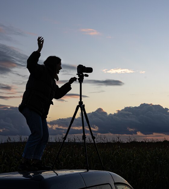 The girl on the roof of the car photographs the sunset with a tripod