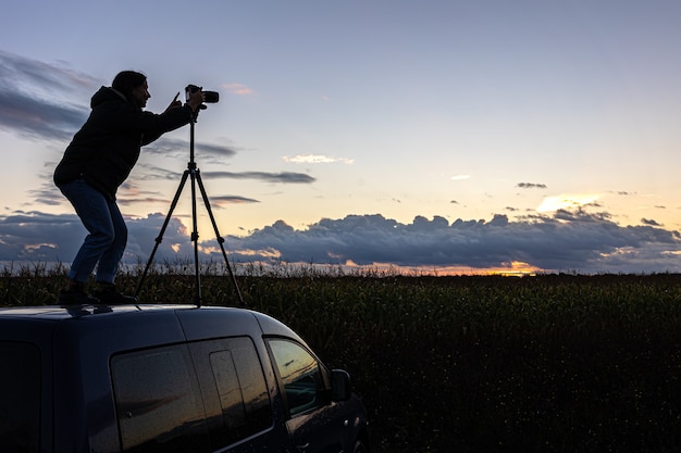 The girl on the roof of the car photographs the sunset with a tripod