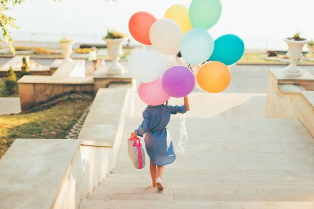 다채로운 풍선과 유치 가방을 들고 계단에서 실행하는 소녀