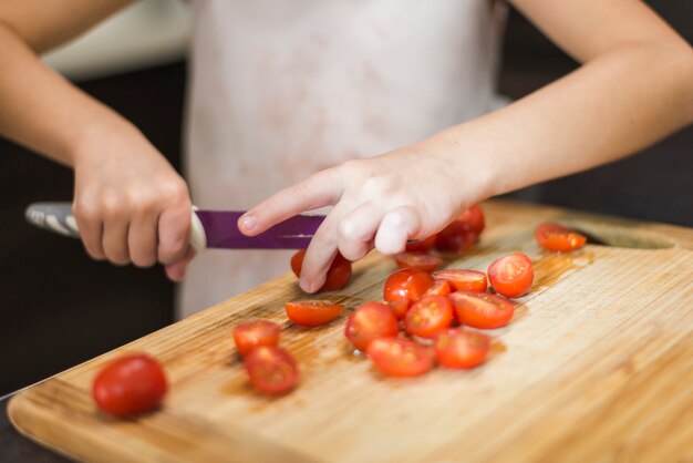 Girl's hand cutting tomatoes on wooden chopping board with knife