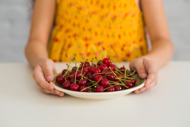 Girl's hand holding red cherries on plate over the white desk