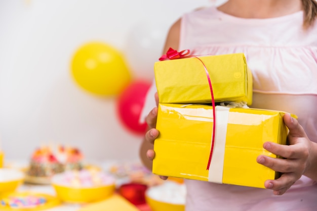 Girl's hand holding yellow gift boxes with red ribbon