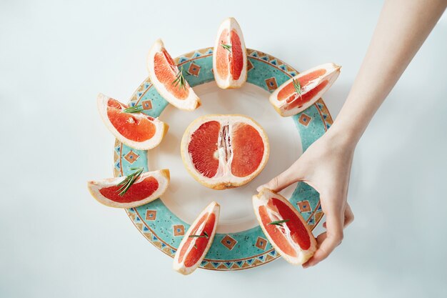 Free photo girl's hand taking slice of grapefruit from white plate. from above. healthy diet nutrition.