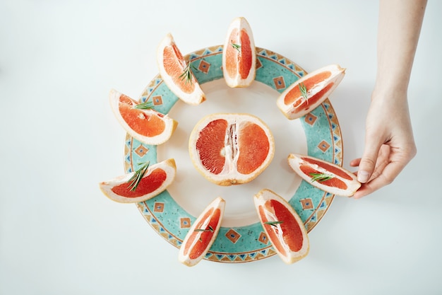 Girl's hand taking slice of grapefruit from white plate. From above. Healthy diet nutrition.