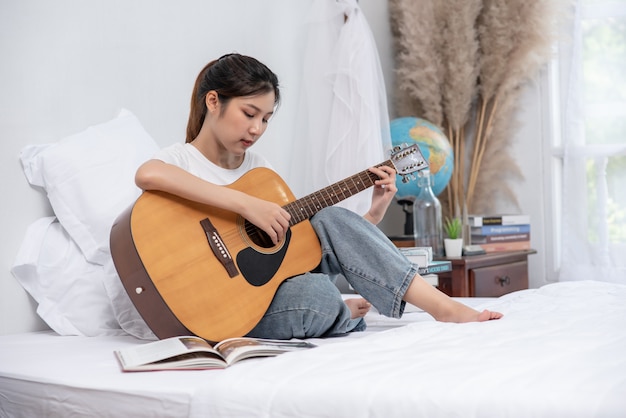 Foto gratuita la ragazza si sedette e suonò la chitarra sul letto.