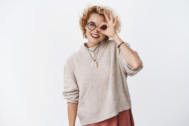 Girl seeks what future holds Portrait of cute and enthusiastic playful pleasant woman in sweater and glasses tilting head showing okay gesture on eye and looking through it joyfully
