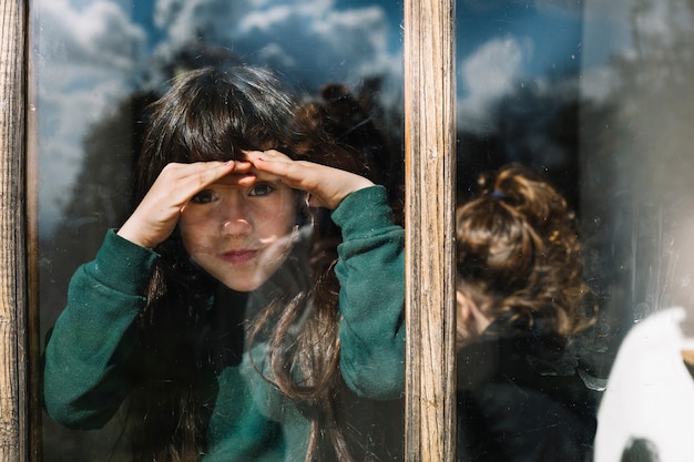 Ragazza che la protegge occhi mentre guarda attraverso la finestra di vetro