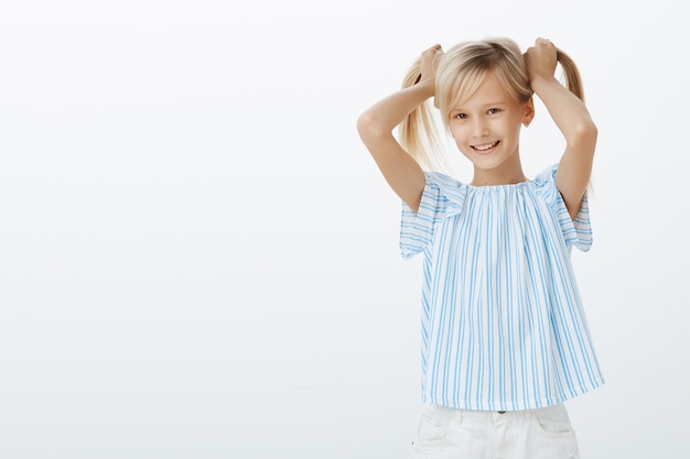 Ragazza che mostra agli amici i suoi nuovi orecchini. gioiosa bambina contenta con i capelli biondi, sollevando i capelli e sorridendo con gioia