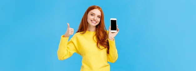 좋은 앱을 보여주는 소녀는 매우 유용한 앱 다운로드를 권장합니다 노란색 sweate에 귀여운 빨간 머리 여자