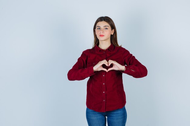 Girl showing heart gesture in burgundy blouse and looking sincere