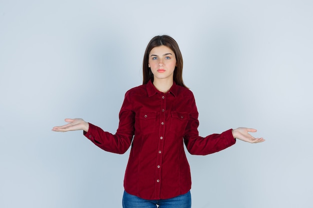 Foto gratuita ragazza che mostra gesto impotente in camicia bordeaux e sembra confusa