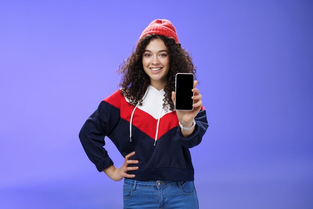 Girl showing her post as pulling smartphone screen towards camera smiling delighted waiting opinion ...