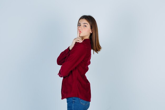 girl showing silence gesture in burgundy shirt and looking mysterious .