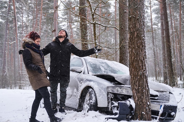 Free photo girl shows her boyfriend the damage to his car after the accident. the girl crashed her boyfriend's car. crashed car after accident in snowy forest