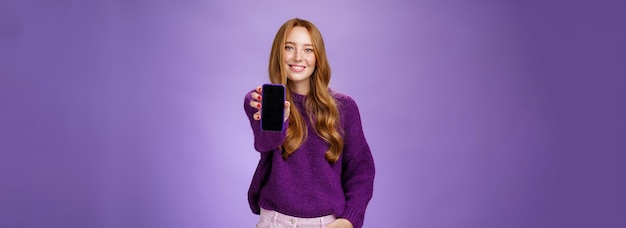 Бесплатное фото Девушка показывает экран смартфона на камеру, чтобы узнать мнение друга, широко улыбающегося с оптимистичным и