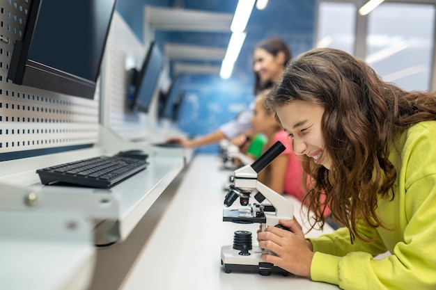 Foto gratuita ragazza lateralmente alla macchina fotografica che esamina il microscopio con interesse