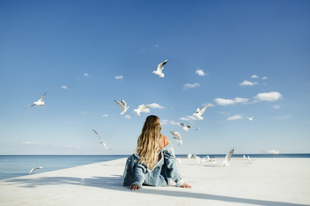 Free photo a girl sits on berth and watch at seagulls