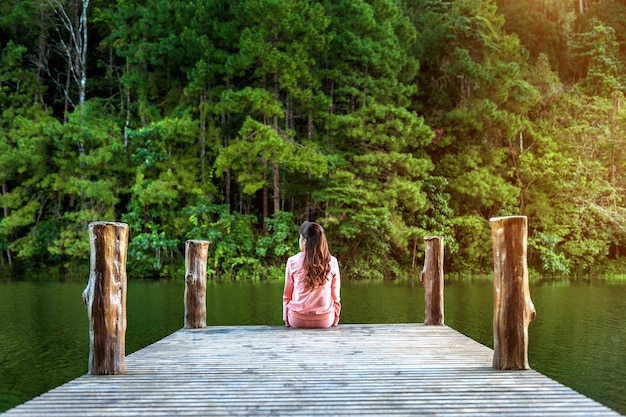 湖の木製の橋に一人で座っている女の子。パンウン、タイ。