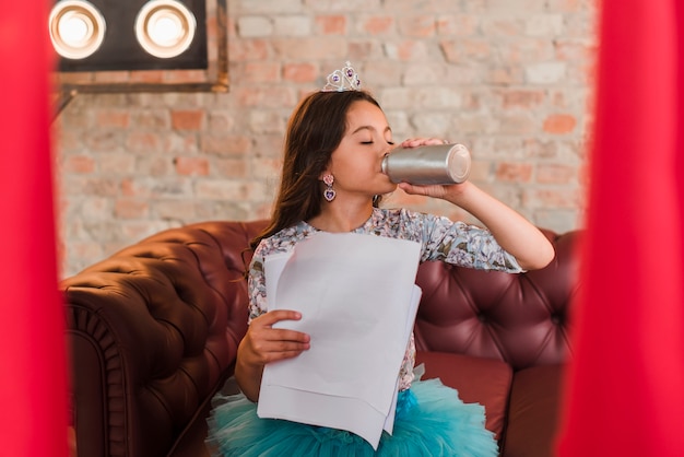 Girl sitting at backstage holding scripts drinking water from bottle