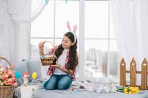 Free photo girl sitting on bed looking at easter eggs basket at home