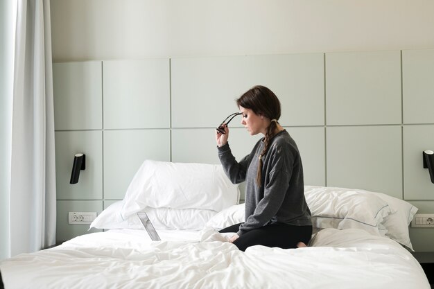 Girl sitting on bed and putting on eyeglasses