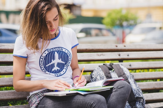 Free photo girl sitting on bench outside making notes