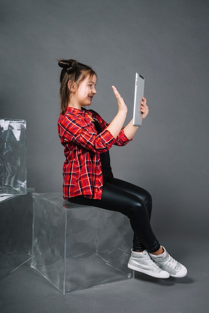 Girl sitting on block having video call through pc tablet waving hand