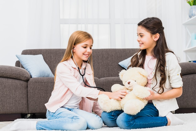 Девушка сидит на ковре, играя с Тедди с помощью стетоскопа в гостиной