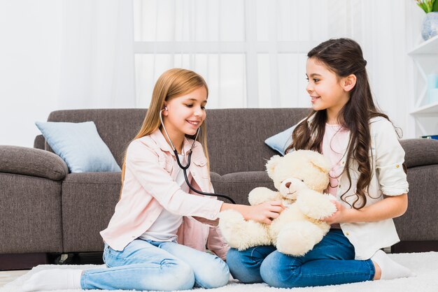 Girl sitting on carpet playing with teddy using stethoscope in the living room