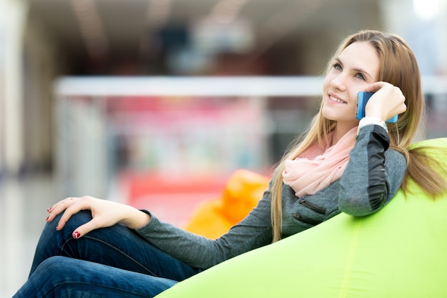 Ragazza che si siede in un divano a parlare sul suo cellulare