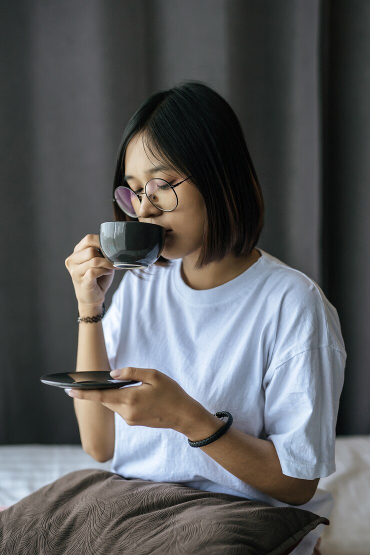 無料Photo 座っていると寝室でコーヒーを飲む女の子。
