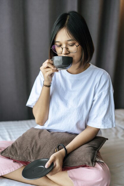 Девушка сидит и пьет кофе в спальне.