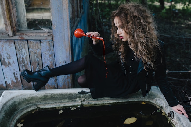 Foto gratuita ragazza seduta sul bordo di una vasca da bagno con una pozione rossa