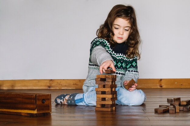 Девушка сидит на полу, укладывая деревянный блок