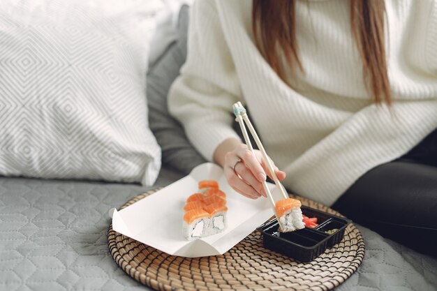 Free photo girl sitting at home on a couch with a sushi