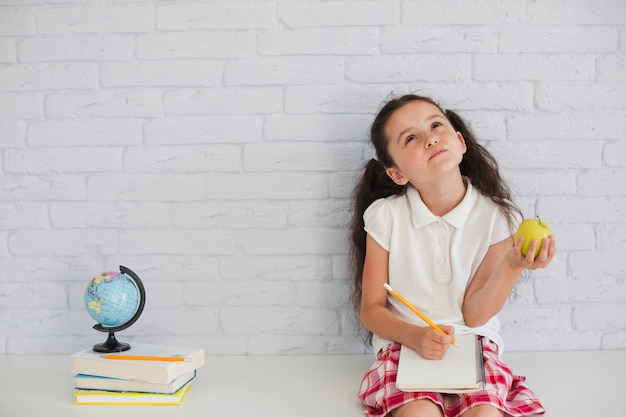 Free photo girl sitting leaning on wall holding apple