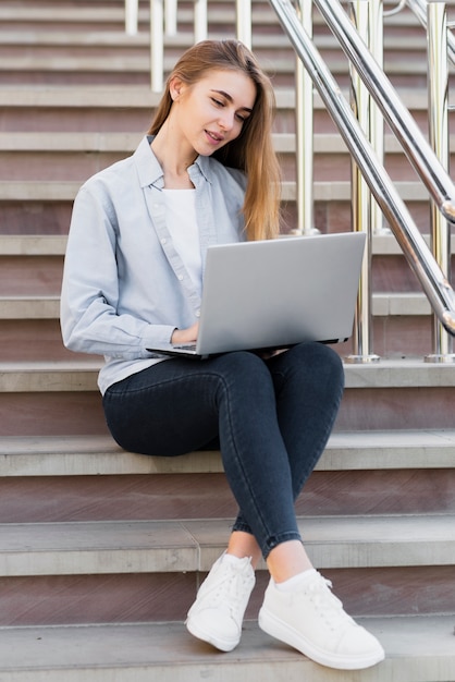 Девушка сидит на лестнице и работает на ноутбуке