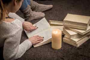 무료 사진 많은 흰색 책과 큰 촛불로 둘러싸인 바닥에 앉아있는 소녀